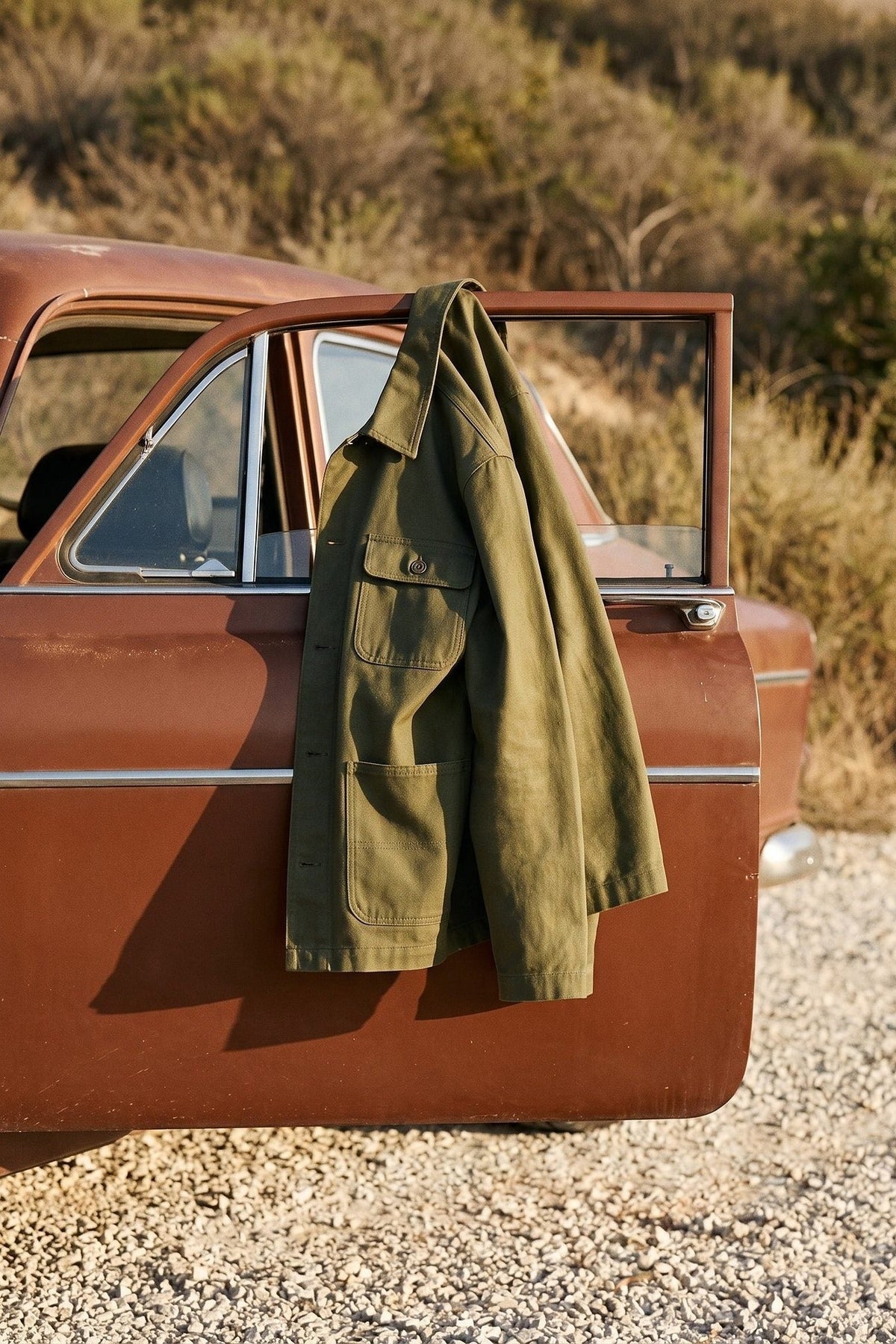Olive green overshirt hung over the open door of a red estate car.
