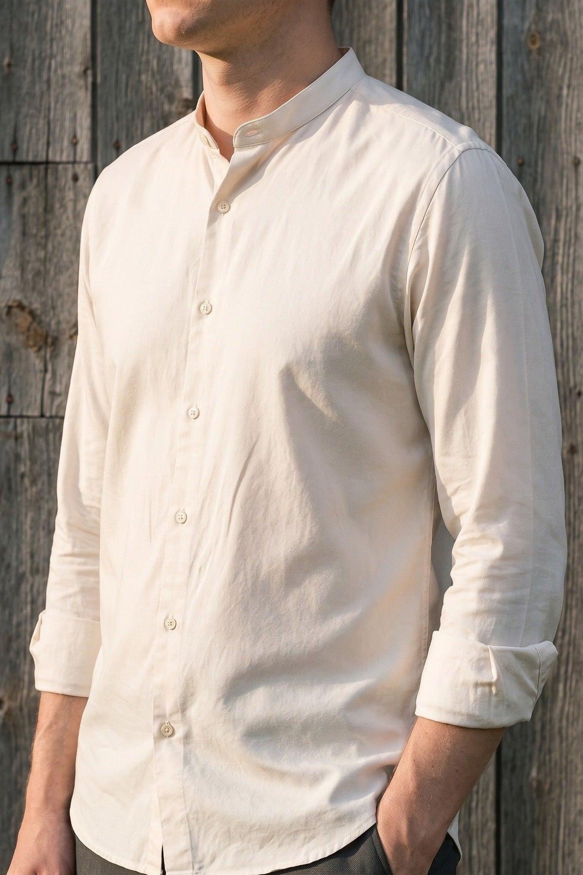 Man in a cream collarless linen shirt against weathered timber boards.