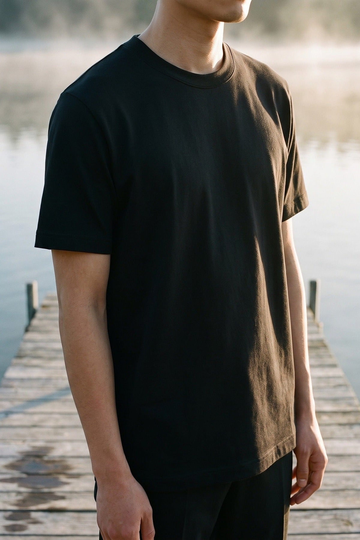 Man in a dark olive T-shirt on a wooden jetty by the water.