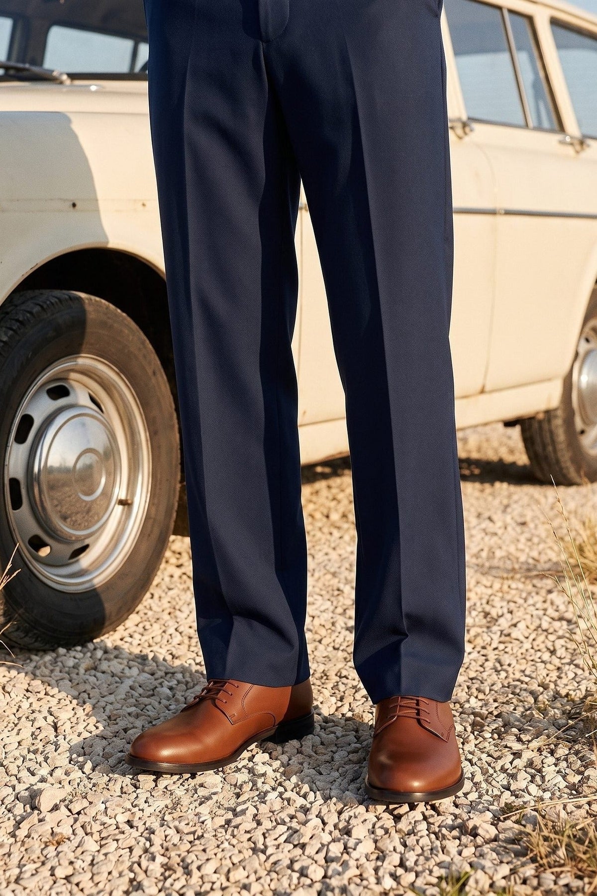 Navy tailored trousers and brown leather derby shoes beside a pale estate car.