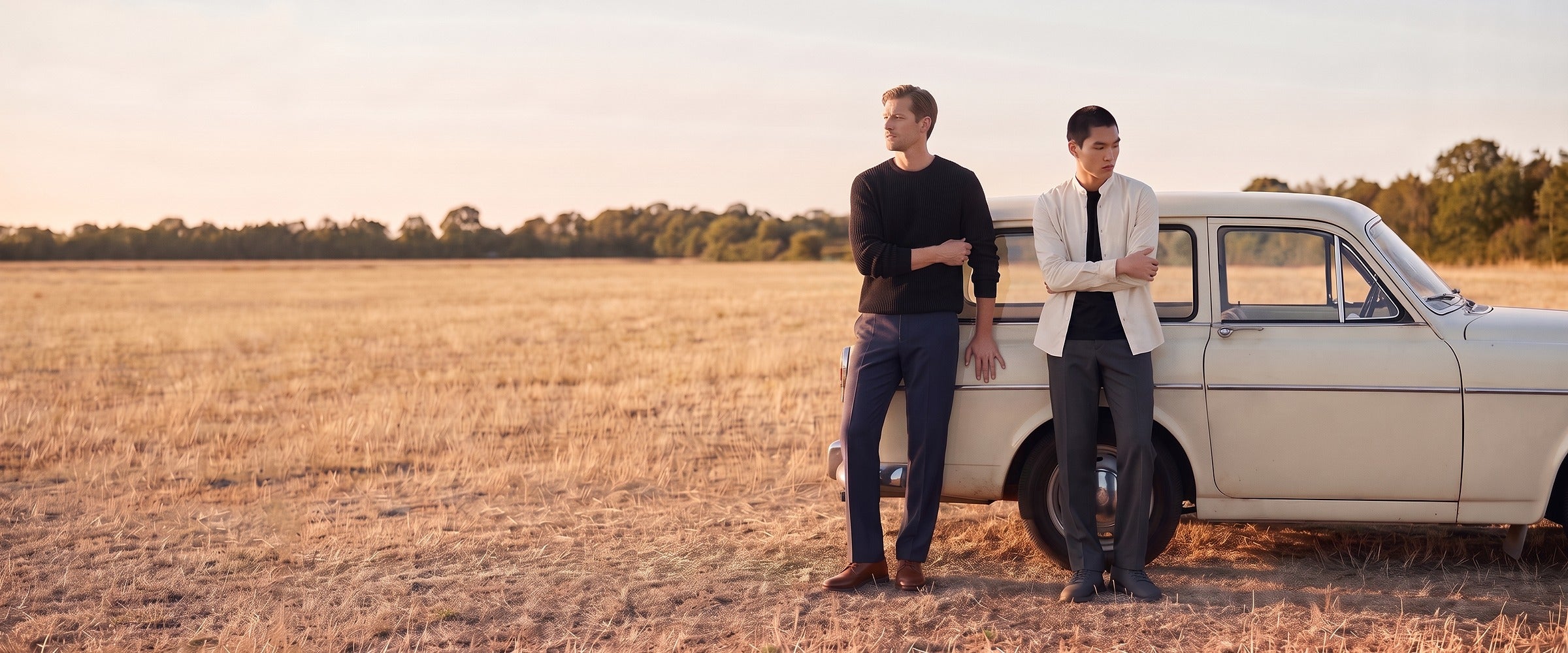 Two men in quiet everyday clothes beside a pale estate car in a golden field at dusk.